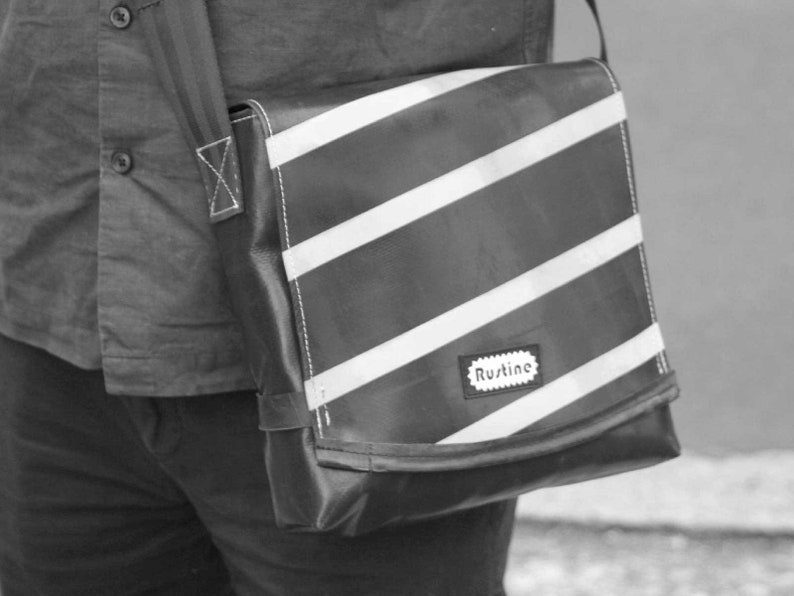 May include: A black and white striped messenger bag with a black strap and a white label that says "Rustine".