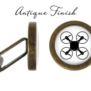 Op de afbeelding: Een paar antieke gouden manchetknopen met een zwart drone-silhouet op een witte achtergrond. De manchetknopen zijn rond en hebben een gladde afwerking.