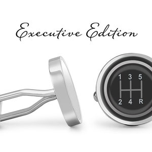 May include: A pair of silver cufflinks with a black and silver gear shift pattern. The cufflinks are labeled "Executive Edition".