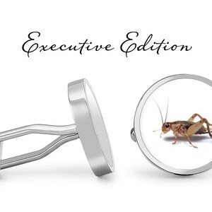 May include: Silver cufflinks with a round, white background featuring a brown cricket. The cufflinks are labeled "Executive Edition".