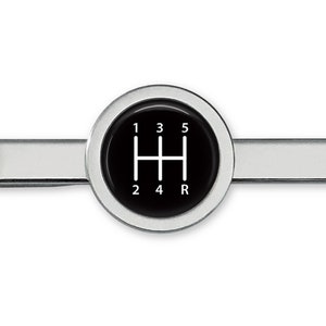 May include: A silver tie clip with a black circular design featuring a white gear shift pattern with the numbers 1, 2, 3, 4, 5, and R.