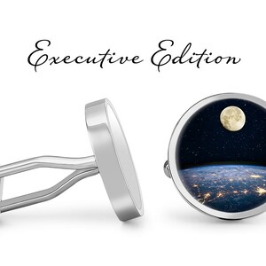 May include: Silver cufflinks with a round design featuring a full moon, stars, and a view of Earth from space. The text "Executive Edition" is written above the cufflinks.