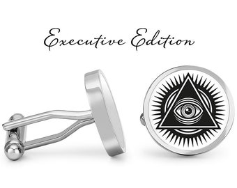 Puede incluir: Un par de gemelos de plata con un diseño de ojo que todo lo ve en blanco y negro. Los gemelos presentan un diseño circular con un triángulo y un ojo en su interior. El texto "Executive Edition" está por encima de los gemelos.