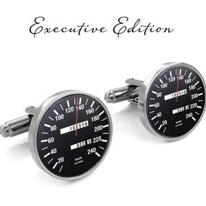 May include: A pair of silver cufflinks shaped like car speedometers. The speedometers have black faces with white numbers and a red needle. The cufflinks are labeled "Executive Edition".