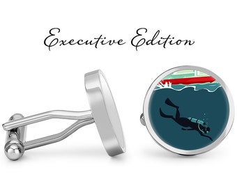 May include: Silver cufflinks with a round blue background featuring a silhouette of a scuba diver with a red and green boat in the background. The text "Executive Edition" is above the cufflinks.