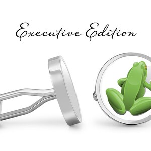 May include: Silver cufflinks with a green frog design. The cufflinks are oval shaped and have a polished finish. The frog is depicted in a realistic style and is facing to the right. The text "Executive Edition" is written above the cufflinks.