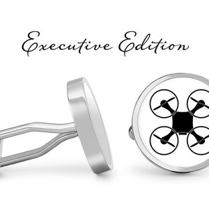 Op de afbeelding: Een paar zilveren manchetknopen met een witte achtergrond en een zwart drone-silhouet. De manchetknopen zijn gelabeld "Executive Edition".