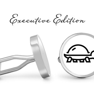 May include: A pair of silver cufflinks with a white background and a black outline of a turtle. The cufflinks are labeled "Executive Edition".