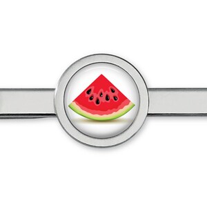 May include: A silver tie bar featuring a round design of a watermelon slice. The watermelon is red with black seeds and a green rind.