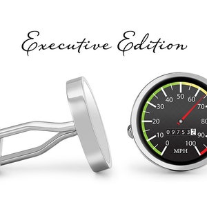 May include: A pair of silver cufflinks with a black and white speedometer design. The speedometer has a green, yellow, and red color scheme and reads "Executive Edition" and "MPH".