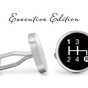 May include: Silver cufflinks with a black face featuring a white gear shift pattern. The text "Executive Edition" is above the cufflinks in a script font. The cufflinks are a classic accessory.