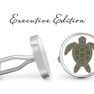 Può includere: Gemelli d'argento con sfondo bianco rotondo e un design di tartaruga marina verde. I gemelli sono etichettati "Executive Edition".