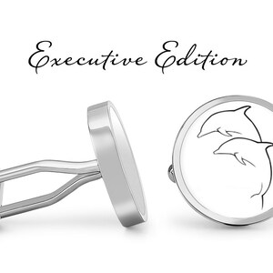 May include: A pair of silver cufflinks with a white enamel design of two dolphins jumping. The cufflinks are labeled "Executive Edition".