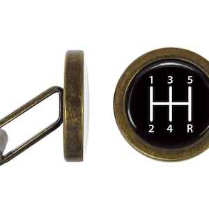 May include: A pair of antique gold cufflinks with a black background and a white gear shift pattern. The numbers 1, 2, 3, 4, 5, and R are displayed on the gear shift pattern.