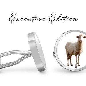 Pode incluir: Um par de botões de punho de prata com uma imagem de ovelha branca em um botão de punho. Os botões de punho são etiquetados como "Executive Edition".