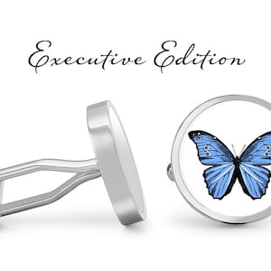 May include: A pair of silver cufflinks with a blue butterfly design. The cufflinks are round and have a white background. The text "Executive Edition" is written above the cufflinks.
