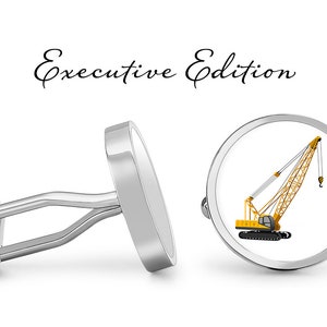 May include: A pair of silver cufflinks with a yellow crane design. The cufflinks are round and have a white background. The text "Executive Edition" is written above the cufflinks.