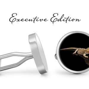 Può includere: Un paio di gemelli d'argento con uno sfondo rotondo nero che presenta una lucertola barbuta. I gemelli sono etichettati "Executive Edition".