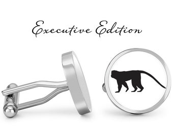 May include: Silver cufflinks with a round, white background and a black silhouette of a monkey. The cufflinks are labeled "Executive Edition".