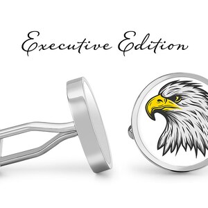 May include: Silver cufflinks with a white background and a black and white illustration of an eagle's head with a yellow beak and eye. The cufflinks are labeled "Executive Edition".