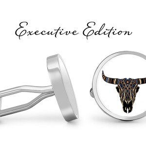 May include: A pair of silver cufflinks with a white background and a black and gold bull skull design. The cufflinks are labeled "Executive Edition".
