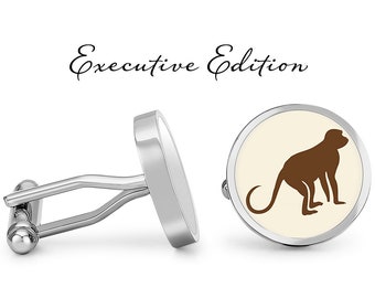 May include: Silver cufflinks with a white background and a brown monkey silhouette. The cufflinks are labeled "Executive Edition".
