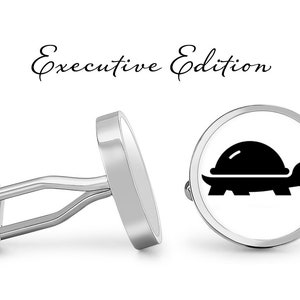May include: Silver cufflinks with a black turtle design on a white background. The words "Executive Edition" are written in cursive above the cufflinks. The cufflinks are round with a shiny finish.