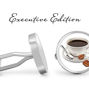 Könnte beinhalten: Silberne Manschettenknöpfe mit einem runden Design, das eine weiße Kaffeetasse mit schwarzem Kaffee und Kaffeebohnen auf einem weißen Unterteller zeigt. Der Text "Executive Edition" befindet sich über den Manschettenknöpfen.