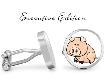 May include: A pair of silver cufflinks with a cartoon pig design. The cufflinks are round and have a white background with a pink pig in the center. The text "Executive Edition" is written above the cufflinks.