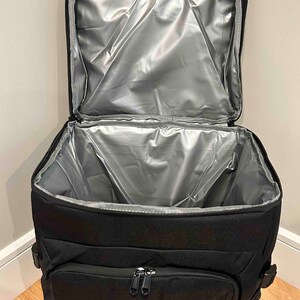 May include: Black insulated cooler bag with a zippered pocket and a silver lining. The bag is open and the lining is visible.