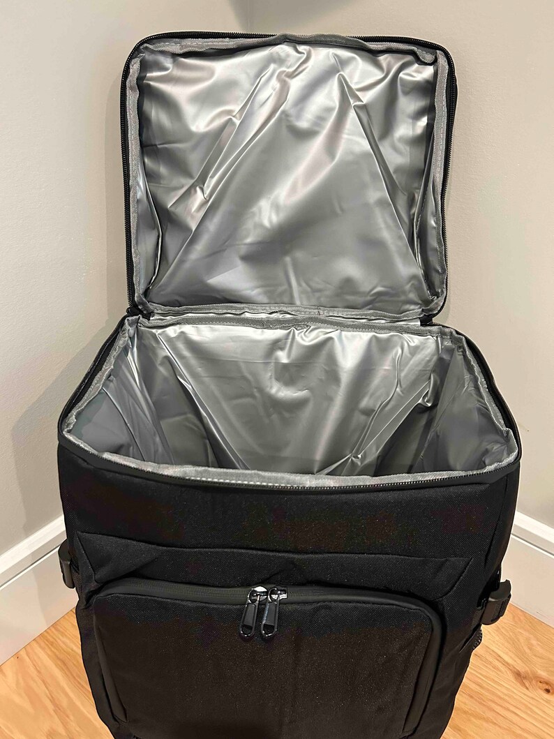 May include: Black insulated cooler bag with a zippered pocket and a silver lining. The bag is open and the lining is visible.