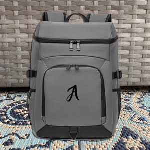 May include: A gray backpack with a black zipper and a black letter "A" embroidered on the front.