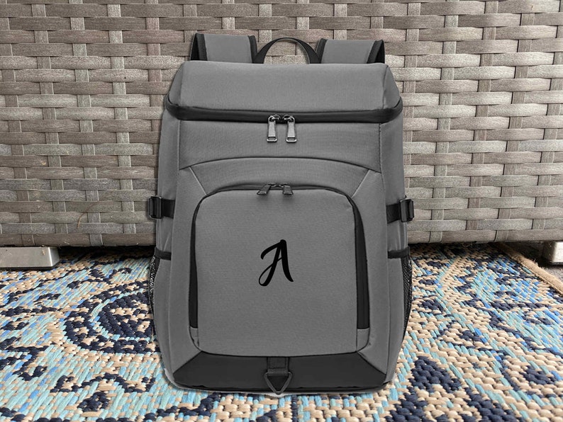 May include: A gray backpack with a black zipper and a black letter "A" embroidered on the front.