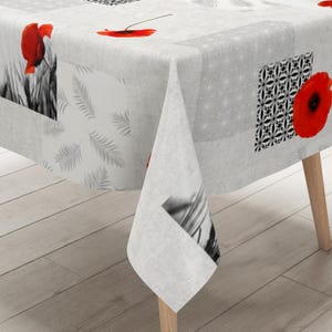 Op de afbeelding: Een rechthoekig tafelkleed met een patchworkontwerp van zwart-witte patronen, waaronder varenbladeren en geometrische vormen, geaccentueerd met felrode klaprozen. De stof hangt over een tafel met lichtgekleurde houten poten.