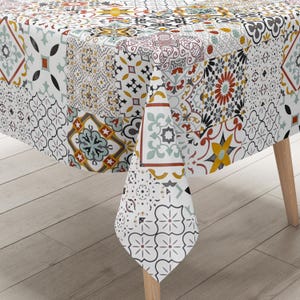 Puede incluir: Un mantel blanco con un diseño de patchwork con varios patrones geométricos y florales en tonos de rojo, azul, amarillo y negro. El mantel está sobre una mesa de madera.