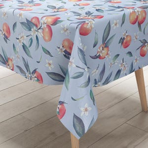 Op de afbeelding: Een lichtblauw tafelkleed met een herhalend patroon van oranje fruit, groene bladeren en witte bloemen.