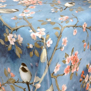 Op de afbeelding: Een blauwe tafelkleed met een bloemenpatroon met roze bloesems en goudkleurige takken. Twee kleine vogels zitten op de takken.