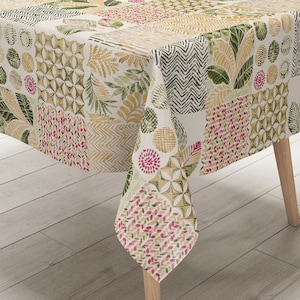 Op de afbeelding: Een rechthoekig tafelkleed met een patchwork-ontwerp met verschillende geometrische patronen en bladmotieven in tinten groen, geel en roze.