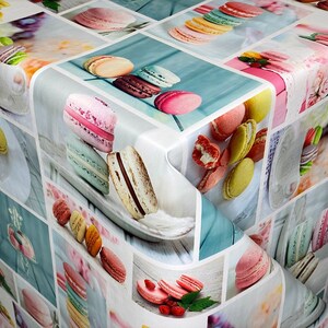 Può includere: Una tovaglia bianca con un motivo colorato di macarons. I macarons sono disposti in vari motivi e colori, tra cui rosa, blu, verde, giallo e marrone. La tovaglia è perfetta per un tè o un'occasione speciale.