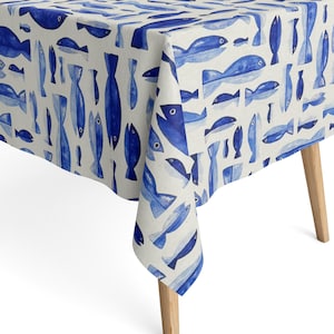 Peut inclure: Une nappe blanche ornée d'un motif répétitif de poissons bleus de style aquarelle, de tailles et d'orientations variées. Le tissu recouvre les bords d'une table et présente un imprimé cohérent de créatures aquatiques peintes à la main.