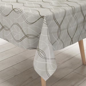 Peut inclure: Une nappe grise et marron avec un motif abstrait ondulé. La nappe est drapé sur une table en bois.