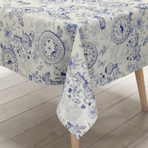 Könnte beinhalten: Eine weiße Tischdecke mit einem blauen und weißen Blumenmuster mit stilisierten Vasen und Tellern. Die Tischdecke ist über einen Tisch mit Holzbeinen gelegt.