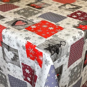 Könnte beinhalten: Eine weiße Tischdecke mit Patchwork-Muster aus roten, burgunderroten und grauen Quadraten mit Schneeflocken und anderen winterlichen Mustern. Die Tischdecke ist aus strapazierfähigem, wasserabweisendem Material.