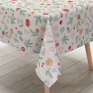 Op de afbeelding: Een witte tafelkleed met een feestelijk patroon met groene dennennaalden, rode bessen en gouden en rode ornamenten. Het tafelkleed is over een houten tafel gedrapeerd en creëert een seizoensgebonden en decoratieve uitstraling.
