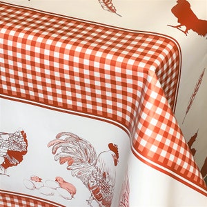 Op de afbeelding: Een witte tafelkleed met een rood-wit ruitpatroon en een rand. Het tafelkleed heeft illustraties van hanen, kippen, eieren en veren. Het ontwerp doet denken aan een boerderij of een landelijke keuken.