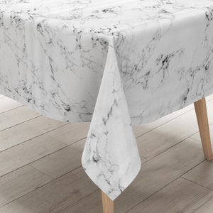 Op de afbeelding: Wit tafelkleed met een marmerpatroon. Het tafelkleed is over een houten tafel gelegd.