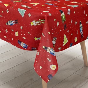 Op de afbeelding: Rode tafelkleed met een kerstnootkrakerpatroon. Het tafelkleed heeft een herhalend patroon van notenkrakers, kerstboom, sterren en sneeuwvlokken.