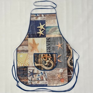 Könnte beinhalten: Eine blaue und weiße Küchenschürze mit nautischem Thema. Die Schürze zeigt verschiedene maritime Designs, darunter Seesterne, Muscheln und ein Seil-Design. Die Schürze hat eine große Tasche auf der Vorderseite.