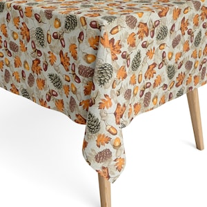 Könnte beinhalten: Eine beige Tischdecke mit einem sich wiederholenden Muster aus Herbstblättern, Eicheln und Tannenzapfen in Orange-, Braun- und Grüntönen. Die Tischdecke ist über einem Holztisch drapiert und zeigt das saisonale Design.