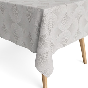 Könnte beinhalten: Ein hellgraues Tischtuch mit einem sich wiederholenden Muster aus sich überlappenden, halbkreisförmigen Formen. Das Tischtuch ist über einem Holztisch mit hellfarbigen Beinen drapiert. Das Design erzeugt einen strukturierten, geschichteten Effekt.